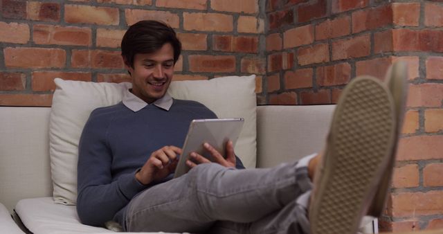 Young man relaxing on sofa using digital tablet - Download Free Stock Images Pikwizard.com