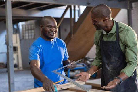 African american carpenters collaborating in workshop measuring plank with square and tape