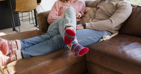 Couple reclining on brown leather sofa wearing colorful patterned socks and knit sweaters
