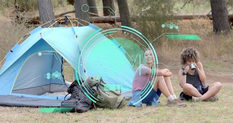 Camping duo sitting by light-blue tent with futuristic HUD overlay, backpacks and mugs