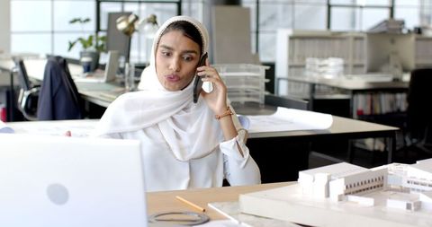 Female Architect Engaged on Laptop While Managing Phone Call in Sleek Office