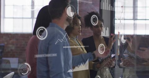 Collaborating team analyzing interactive data visualizations on glass wall in modern office