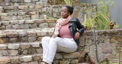 Contemplative African American Woman Sitting on Stone Steps Wearing Scarf and Leather Jacket