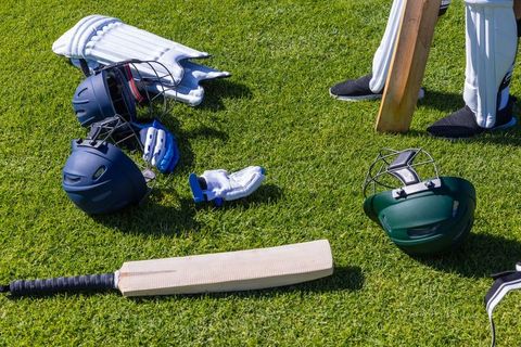 Sunlit cricket gear laid on grass, bats, helmets, gloves and pads prepping for match