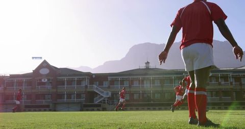 Youth soccer players sprinting across sunlit grass field near brick school building