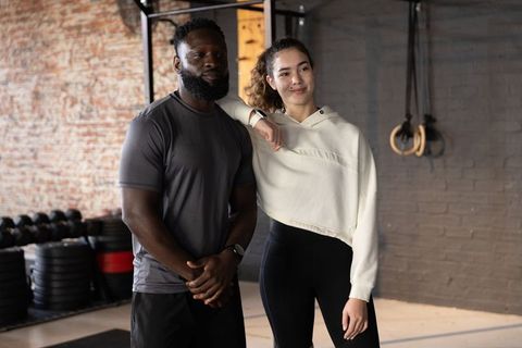 Diverse gym partners posing together leaning on shoulder near weight plates and rings