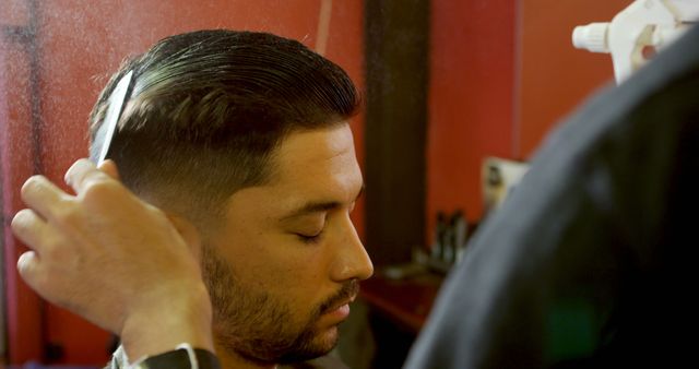 A young Latino man is getting a haircut in a barbershop, with copy space. His hair is being styled with precision, showcasing a moment of personal grooming and care.