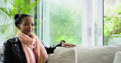 African American woman sitting on sofa near glass doors wearing leather jacket and scarf