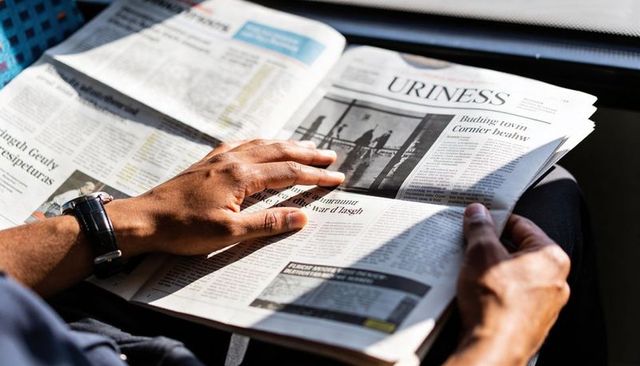 Man reading morning newspaper in car sunlit hands flipping broadsheet with wristwatch
