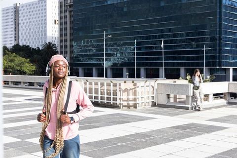 African-american teen listening to music walking through urban plaza in pink hoodie