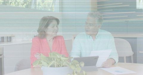 Couple discussing household finances at sunlit kitchen table with tablet and paperwork