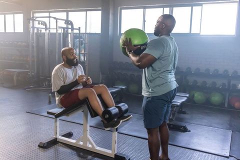 African american men training together passing medicine ball on decline ab bench in gym
