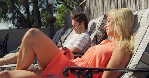 Relaxed Couple Lounging by Pool Enjoying Smartphone