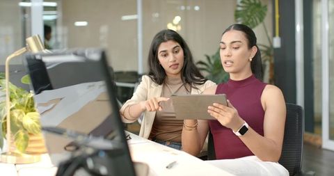 Female Colleagues Collaborating Over Tablet in Bright Open Office Space for Teamwork and Productivit