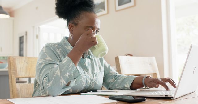 Middle-aged woman drinking coffee while working on laptop at home - Download Free Stock Images Pikwizard.com