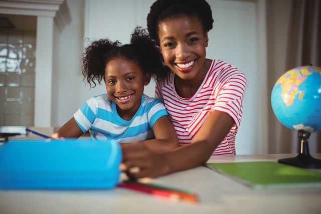 Mother assisting her daughter with homework. Both are smiling, creating a positive and supportive learning environment at home. Could be used for content related to family bonding, education, or parenting tips.