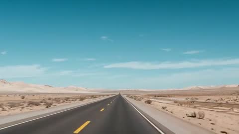 Driving along endless desert highway toward distant dunes under clear turquoise sky