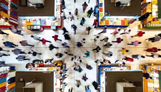 Overhead view of busy indoor market with shoppers walking amid colorful stalls and produce