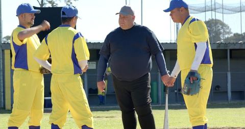 Senior baseball players consulting umpire between innings on sunny community ballpark