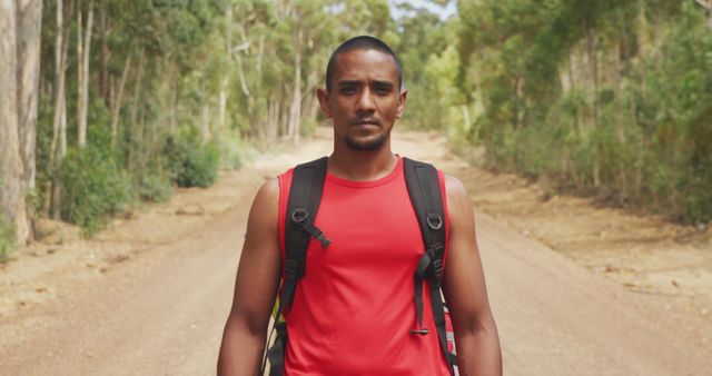 Man wearing red backpack walking along forest trail. Ideal for themes of outdoor adventure, nature exploration, fitness, and healthy lifestyle.