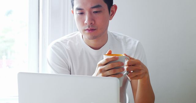 Focused Young Man Holding Coffee Mug While Working on Laptop at Home - Download Free Stock Images Pikwizard.com