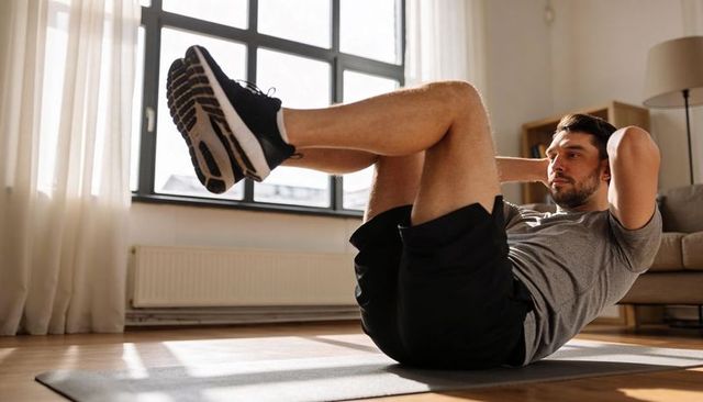 Sunlit living room core workout with adult man performing bicycle crunch on mat in casual sportswear