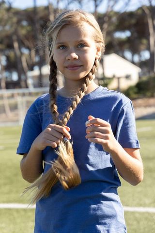 Sunlit girl with braided pigtails standing on soccer field wearing blue shirt
