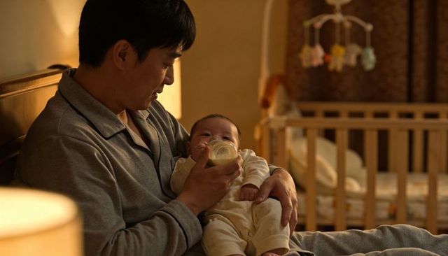 Asian father feeding baby with bottle at night in cozy nursery for bedtime bonding
