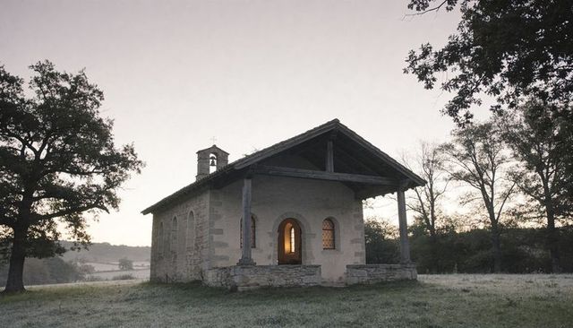 Small stone chapel standing in frosty meadow at twilight with warm lantern glow