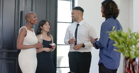 Diverse friends chatting at cocktail party in modern entryway with drinks and sunlight