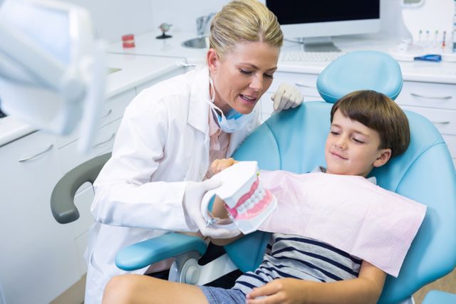Dentist explaining dental care to a young boy using a dental mould in a modern clinic. Ideal for use in healthcare, pediatric dentistry, dental education, and oral health awareness materials.