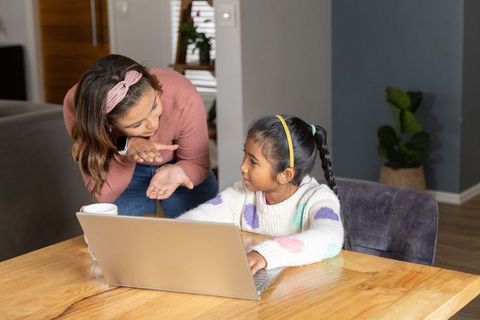 Woman guiding girl on laptop at dining table for online tutoring and remote learning