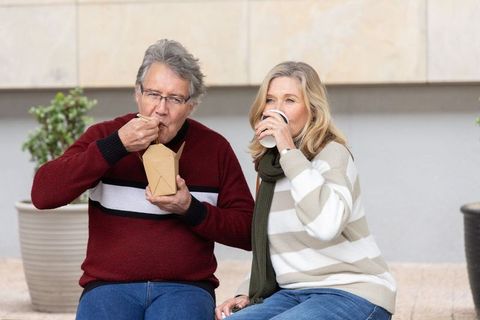 Senior couple enjoying takeout and coffee on urban bench during relaxed city outing