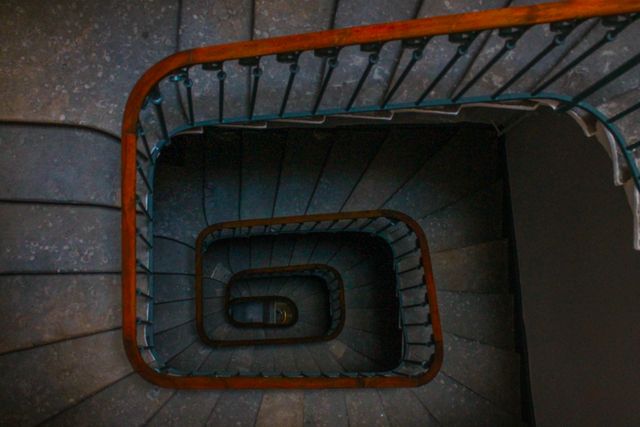 This captivating image features an aerial view of a spiral staircase with a dark patina and ornate wooden handrail. The symmetry and elegant design make this perfect for representing architectural beauty, interior design inspirations, or articles related to architecture. It can also be used in artwork, minimalist designs, or as a background for presentations.