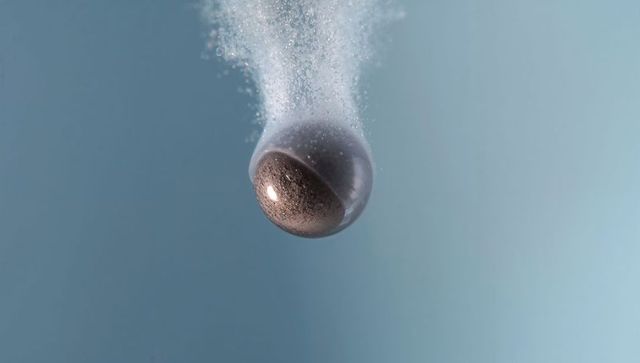 Floating glass sphere with half-rough bronze core releasing microbubbles in aqua liquid