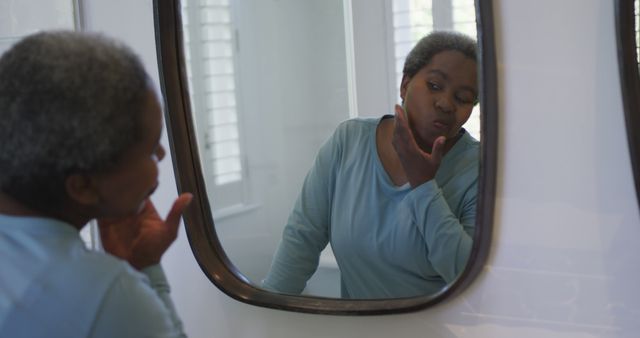 Senior woman inspecting her skin in bathroom mirror. Ideal for articles or advertisements related to skincare routines for mature skin, self-care, health awareness, elderly hygiene routines, or lifestyle of senior women.