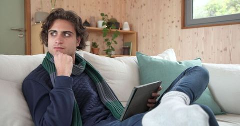 Young Man Relaxing on Sofa Using Tablet in Modern Minimalist Home