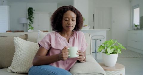 Calm woman relaxing with mug on cozy beige sofa in bright minimalist home interior