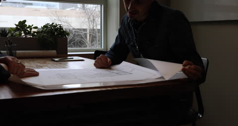 Architects Collaborating and Examining Blueprints in an Office Setting