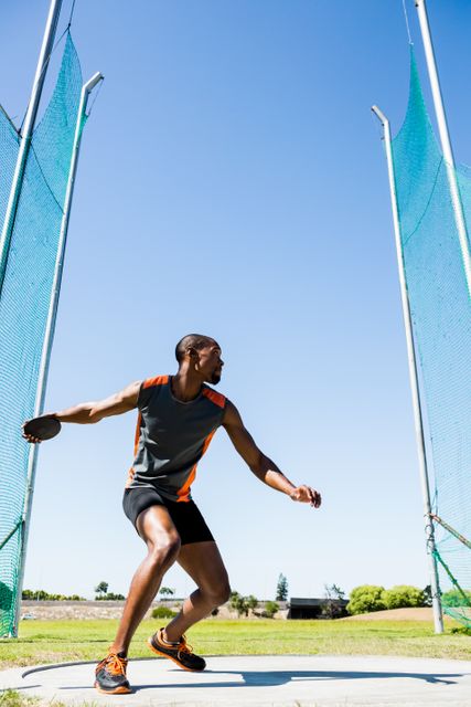 An athlete in athletic gear getting ready to throw a discus in an outdoor stadium setting. Great for use in sports-related articles, fitness and training blogs, athletic competition advertisements, and promotional materials for sports equipment.