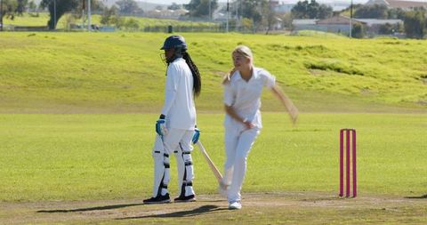 Female Cricket Players on Pitch with Pink Stumps and Helmets