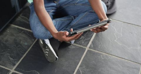Sitting male holding tablet in folio on slate floor wearing jeans and sneakers