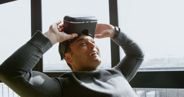 A man enthusiastically holding a VR headset near window in a bright office. Suitable for technology, innovation, modern gadgets themes, or illustrating the excitement of trying virtual reality.
