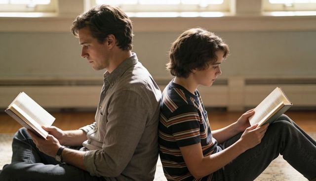 Father and son reading back-to-back on sunlit hardwood floor, quiet family bonding