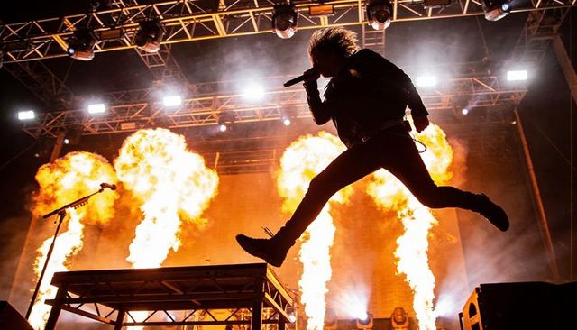 Rock vocalist leaping through flames on high-energy concert stage with pyrotechnics
