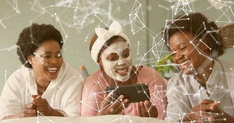 Friends enjoying at-home spa night, relaxing with facial mask and tablet entertainment