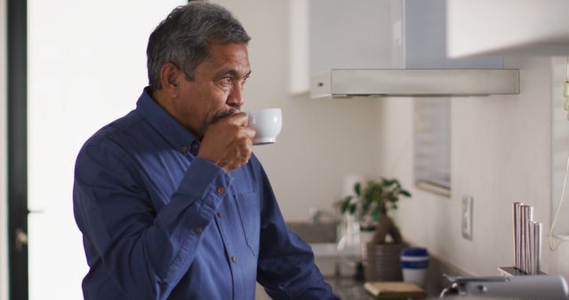 Senior man drinking coffee in modern kitchen scene. Ideal for depicting daily routines, retirement lifestyle, or wellness themes. Suitable for use in advertisements, articles, and promotions related to health, morning routines, or senior living.