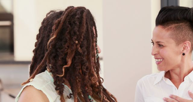 Two women, one with dreadlocks and the other with a short haircut, are engaged in a friendly conversation, with copy space. Their cheerful expressions suggest a positive interaction or a moment of shared humor.