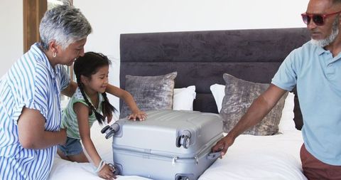 Grandparents and Granddaughter Joyfully Unpacking Suitcase in Modern Bedroom