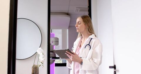 Female clinician holding tablet with stethoscope in clinic doorway with radiology unit